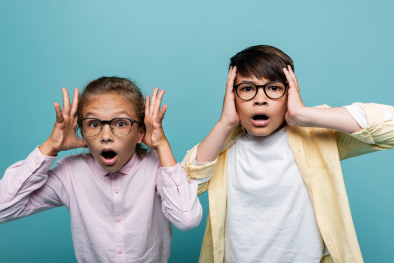 Scared interracial schoolchildren in eyeglasses looking at camera isolated on blue