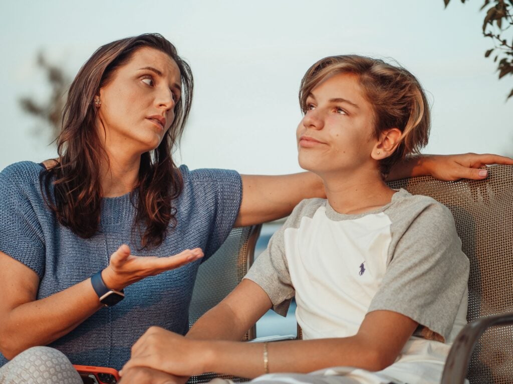 A mother and her teenage son engage in a conversation sitting outside.