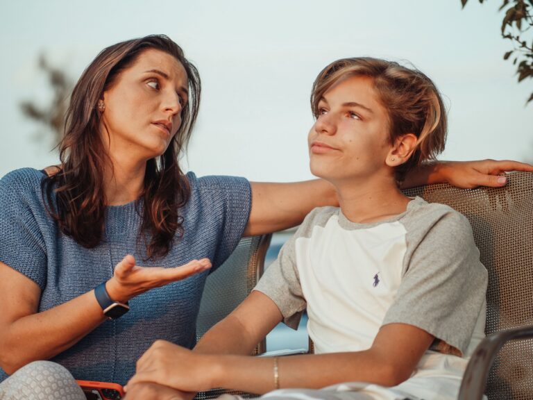 A mother and her teenage son engage in a conversation sitting outside.